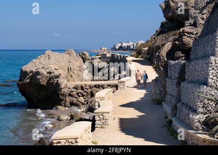 Zwei Touristen gehen Hand in Hand entlang einer Küstenpromenade, einem Pfad oder Kritika in Richtung Altstadt von Rhodos, Rhodos, Griechenland an einem warmen sonnigen Tag Stockfoto