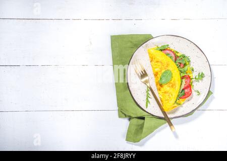 Frühling gesunde Ernährung Lebensmittelkonzept. Rühreier, gefülltes Omelett mit frischem Gemüse, Tomaten, Rucolla, Salat, auf weißem Hintergrund Platz zum Kopieren Stockfoto