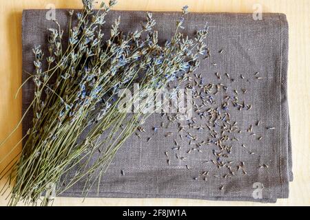 Bouquet von trockenem Lavendel ist auf einfarbigen grauen Leinenstoff. Gefallene kleine Blüten sind abstrakt auf dem Stoff verstreut. Rustikaler Stil. Draufsicht, flach Stockfoto