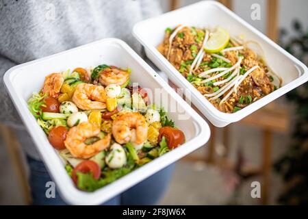 Lebensmittelzustellung ins Büro oder für Picknick in Einweg-Plastikgeschirr. Garnelensalat und asiatisches Pad thai. Stockfoto