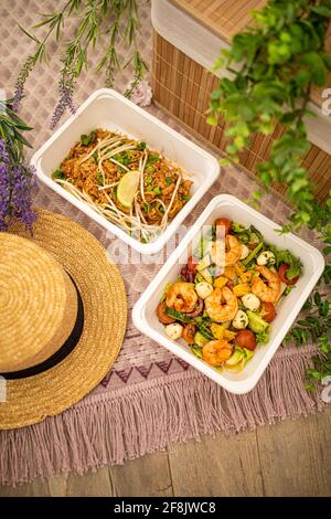 Garnelensalat und asiatisches Pad thai. Zusammensetzung mit natürlichem Dekor. Konzept Lieferung von Lebensmitteln. Picknick im Freien Sommer Frühling Zeit und Plastikgeschirr. Stockfoto