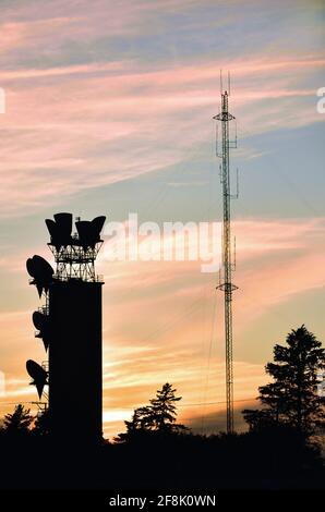 Burlington, Illinois, USA Relais- und Zellentürme werden durch die Hintergrundbeleuchtung der untergehenden Sonne silhouettiert. Stockfoto