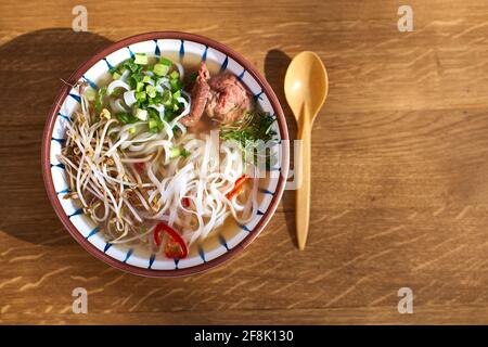 Asiatische Pho bo-Suppe, beste Pho-Brühe, in einer leichten Schüssel auf einem Holztisch, Copy Space, selektiver Fokus, Draufsicht Stockfoto