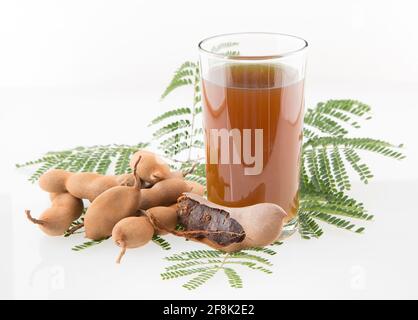 Tamarindensaft in einem Glas, umgeben von frischen reifen Tamarinden - Tamarindus indica Stockfoto