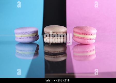 Drei Makronen auf einem blau-schwarz-rosa Hintergrund verschiedene Farben verschiedenen Geschmacksrichtungen mit Platz für Text und Reflexion. Stockfoto