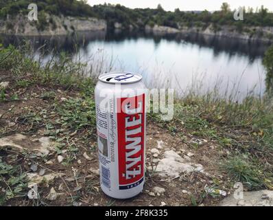 Krakau, Polen - 14. April 2021: Eine beliebte polnische Bierkutte auf Gras im Freien namens Zywiec, die bei bewölktem Wetter vor einem natürlich geformten See gehalten wird Stockfoto