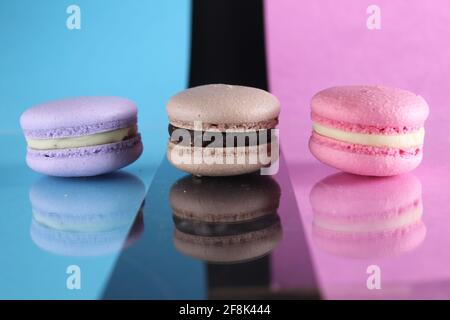 Drei Makronen auf einem blau-schwarz-rosa Hintergrund verschiedene Farben verschiedenen Geschmacksrichtungen mit Platz für Text und Reflexion. Stockfoto