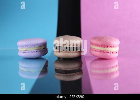 Drei Makronen auf einem blau-schwarz-rosa Hintergrund verschiedene Farben verschiedenen Geschmacksrichtungen mit Platz für Text und Reflexion. Stockfoto