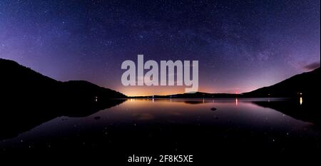 Ein Blick auf den Bassenthwaite See bei Nacht mit einem schwachen milchstraße über dem See und Sterne und Lichter Über den See reflektieren Stockfoto
