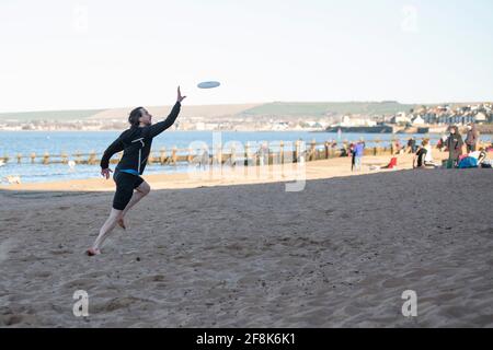 Edinburgh, Schottland, Großbritannien. April 2021. IM BILD: Ein Mann fängt eine fliegende Frisbee am Strand von Portobello. Die Menschen genießen den klaren blauen Himmel und das warme, sonnige Wetter auf der Ostseite Schottlands am Portobello Beach. Quelle: Colin Fisher/Alamy Live News Stockfoto