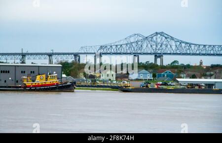 Arbeiten am Ufer des Mississippi River in New Orleans, mit Brücke, Schlepper und Lastkahn. Bunte ältere Häuser am Ufer. Stockfoto