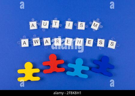 Hintergrund des Welt-Autismus-Bewusstseins-Monats. Transparente Puzzle Details auf Inschrift Autismus Bewusstsein und vier Holzspielzeug auf blauem Hintergrund. Stockfoto