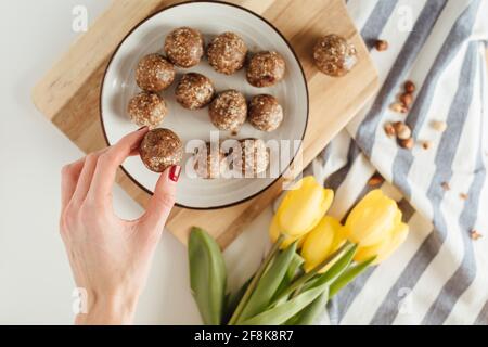 Die Hand der Frau greift nach hausgemachten Schokoladenknäueln, die auf einem Teller mit gelben Tulpen serviert werden. Stockfoto