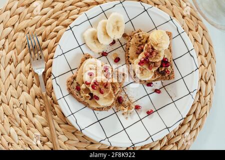 Schuss der Erdnussbutter Toast mit Bananenscheiben und Granatapfel auf einem Teller. Stockfoto