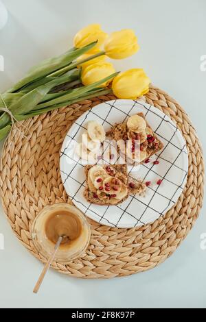 Vertikale Aufnahme der Erdnussbutter Toast mit Früchten auf einem Teller mit gelben Tulpe verziert. Stockfoto