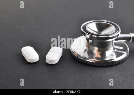 Stethoskop und Pillen auf schwarzer Oberfläche. Diagnose- und Behandlungskonzept. Stockfoto