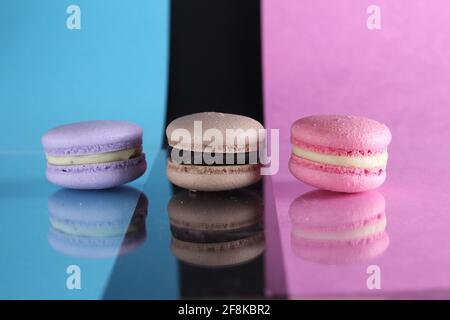 Drei Makronen auf einem blau-schwarz-rosa Hintergrund verschiedene Farben verschiedenen Geschmacksrichtungen mit Platz für Text und Reflexion. Stockfoto