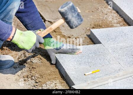 Ein Arbeiter legt mit einem Gummihammer Granitblöcke auf den Bürgersteig. Stockfoto