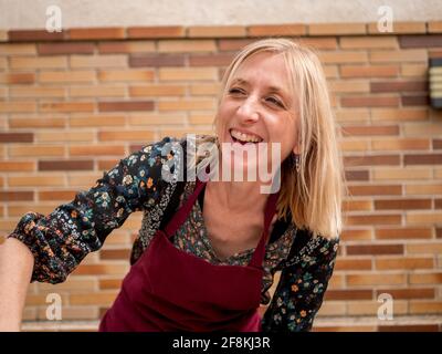 Schöne kaukasische Frau aus Spanien mit roter Schürze lächelnd Der Hinterhof ihres Hauses Stockfoto
