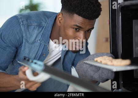 Ein hübscher Mann, der ein Tablett mit gebackenen Plätzchen aus dem Ofen herausnahm Stockfoto