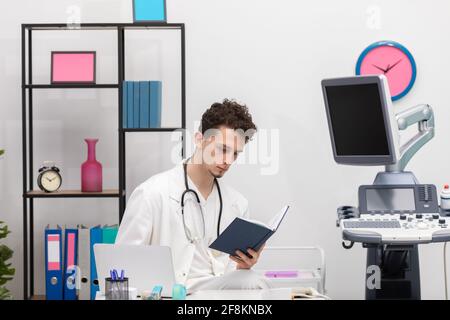 Ein junger Hausarzt überprüft Buchkalendereinträge über seine Patienten. Die Arztpraxis Stockfoto