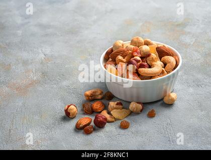 Gesunder Snack: Eine Mischung aus getrockneten Früchten und verschiedenen Nüssen auf grauem Hintergrund. Seitenansicht, Nahaufnahme, Kopierbereich. Stockfoto