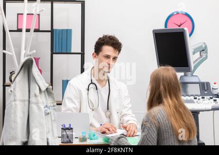 Ein Arzt spricht mit einem Patienten in seiner Arztpraxis. Ein krankes Mädchen im Teenageralter sitzt im Büro ihres Arztes. Grafischer Ultraschall Stockfoto