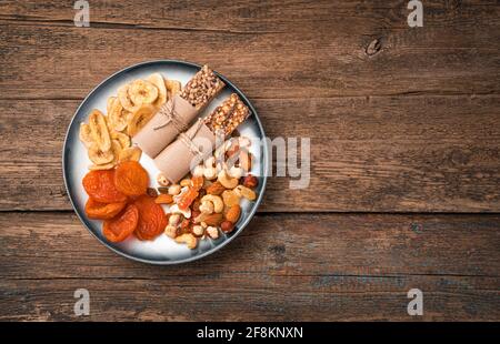 Gesunde, vitaminreiche Snacks auf einem Teller auf Holzboden. Müsliriegel, Auswahl an Nüssen und getrockneten Früchten. Stockfoto
