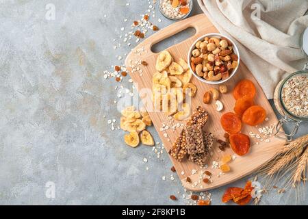 Vitaminreiche, gesunde natürliche Süßigkeiten auf grauem Hintergrund. Müsliriegel, Nüsse und getrocknete Früchte auf einem Holzbrett. Draufsicht, Kopierbereich. Stockfoto