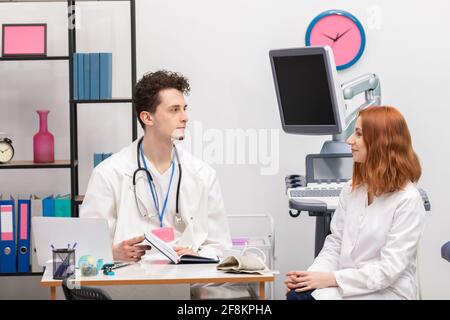 Ein Arzt spricht mit einer Krankenschwester in seinem Büro, während er auf den nächsten Patienten wartet. Hausarzt Stockfoto