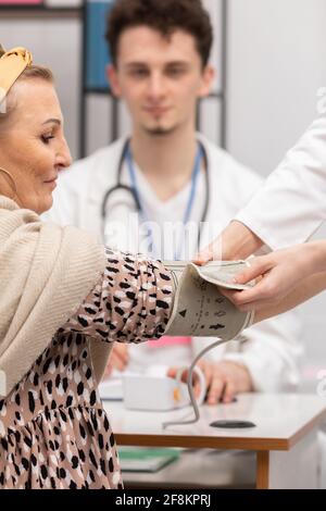 Nahaufnahme einer Krankenschwester, die einen 50-jährigen Patienten mit einem Blutdruckmessgerät versorgt. Arztpraxis Stockfoto