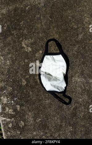 Vertikale Aufnahme der Baumwollmaske auf Betonstraße weggeworfen. Stockfoto