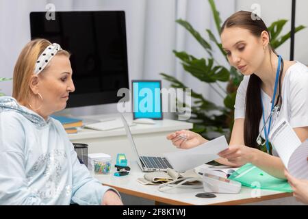 Der Arzt erklärt dem Patienten nacheinander die verschiedenen Testergebnisse. Eine 50-jährige Frau in einem Rollstuhl in der Arztpraxis. Stockfoto