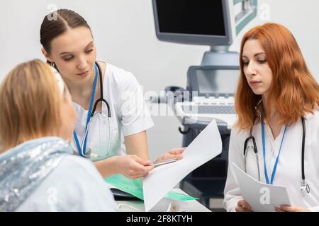 Der Arzt erklärt dem Patienten nacheinander die verschiedenen Testergebnisse. Eine 50-jährige Frau in einem Rollstuhl in der Arztpraxis. Stockfoto