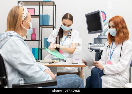 Ein Arzt nimmt die Krankenakten ihrer Patientin heraus. Eine 50-jährige Frau in einem Rollstuhl in der Arztpraxis Stockfoto