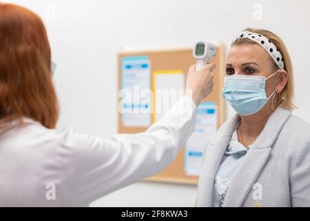 Eine rothaarige Krankenschwester steht am Eingang der Klinik Und überprüft die Temperatur der eintreffenden Patienten, um diese zu eliminieren Infiziert mit COVID-19 Stockfoto