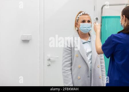 Eine Krankenschwester steht am Eingang der Klinik und Überprüft die Temperatur der eingehenden Patienten, um die Infizierten zu eliminieren Mit COVID-19 Stockfoto
