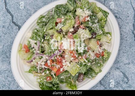 Blick von oben auf den griechischen Salat, der sich auf einem Pappteller mit Rosensalat, Fetakäse, Gurke und Dressing auftürmte, um jeden Appetit zu füllen. Stockfoto