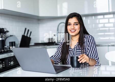 Indische Frau trinkt Kaffee, während sie auf ihrem Laptop ist. Arbeiten von zu Hause aus in Quarantänesperre. Soziale Distanzierung Selbstisolierung Stockfoto