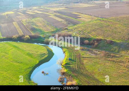 Blick von oben auf fließenden Fluss mit Feldern und Gärten. Rustikales Panorama im Frühling Stockfoto