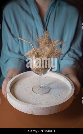 Mädchen in Kimono mit Pampas-Gras-Cocktail in einem Glas mit einem Stroh aus Pampas-Stiel auf einem Teller. Minimale abstrakte Komposition Hintergrund. Stockfoto