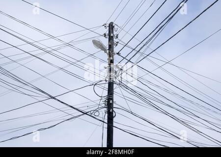 Land Line chaotische schwarze elektrische Kabel Kabel auf elektrischen Stangen. Gegen den bewölkten Himmel Stockfoto