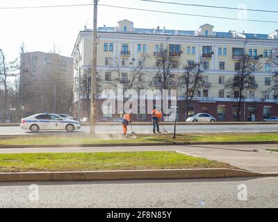 Moskau. Russland. 06. April 2021. Orangefarbene uniformierte Hausmeister, die auf einer Straße in der Stadt den Rasen fegen. Sonniger Frühlingstag. Die Arbeit der Gemeinde Stockfoto