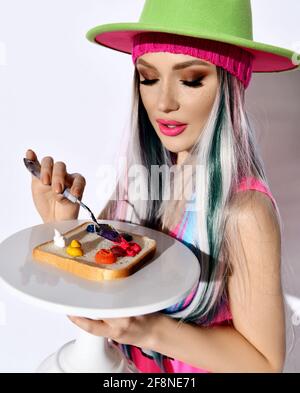 Porträt einer jungen Frau moderne Künstlerin in rosa Hemd und Grüner Hut schmiert Ölfarben auf dem Stück Brot Mit Spachtel Stockfoto