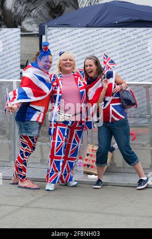 Drei Frauen, die Union Jack tragen und Teil einer großen Menschenmenge sind, versammelten sich auf dem Trafalgar Square, um einen riesigen Fernseher zu sehen, der ihre Königliche Hoheit, Königin Elizabeth ii, die Feierlichkeiten zum Diamantenjubiläum zeigt. Trafalgar Square, London, Großbritannien. 5 Juni 2012 Stockfoto