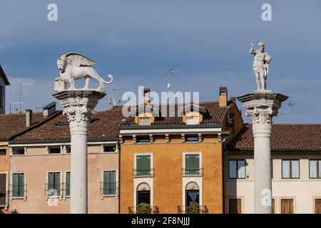 Statue eines geflügelten Löwen und eines Männchens auf dem Säulenoberseite im Hintergrund von Gebäuden in Italien Stockfoto