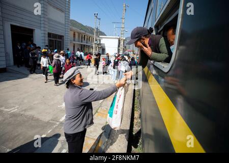 (210415) -- XICHANG, 15. April 2021 (Xinhua) -- EIN Passagier der ethnischen Gruppe Yi macht einen Deal mit einem Hausierer, als der Zug 5633 am 11. April 2021 an einem Bahnhof in der südwestlichen chinesischen Provinz Sichuan anhält. Während moderne Hochgeschwindigkeitszüge an neuen Bahnhöfen in ganz China vorbeifahren, fahren noch immer zwei langsamere Züge durch die Daliang Mountains. Die 5633/5634 Züge verkehren zwischen Puxiong und Panzhihua in der Provinz Sichuan mit einer Durchschnittsgeschwindigkeit von weniger als 40 km pro Stunde. Die Fahrt mit 26 Stationen dazwischen dauert elf Stunden und vier Minuten, die Fahrkartenpreise reichen von 2 Yuan bis 25.5 Yuan(abo Stockfoto