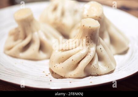 Einige hausgemachte gekochte Khinkali mit Pfeffer auf Keramikplatte, Khinkali ist traditionelles kaukasisches Essen Stockfoto