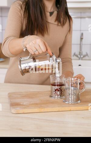 Eine Frau in einer hellen skandinavischen Küche gießt Tee aus Eine Teekannen in einen Becher am Morgen Stockfoto
