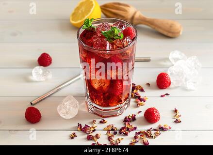 hibiskus-Eistee oder Karkade-Limonade mit Himbeeren, Minze und Zitrone auf einem Holztisch. Stockfoto